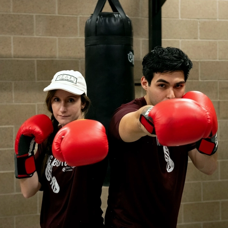 Hai người tạo dáng với găng tay boxing và bao cát phía sau