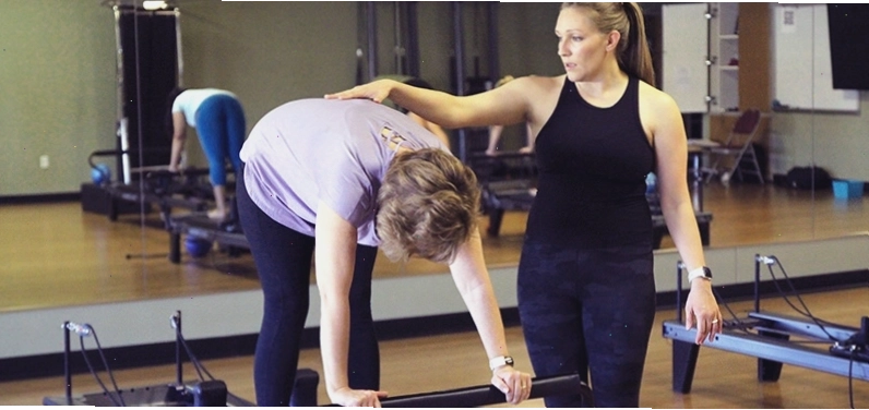 Huấn luyện viên Pilates hỗ trợ học viên nữ trên máy tập reformer