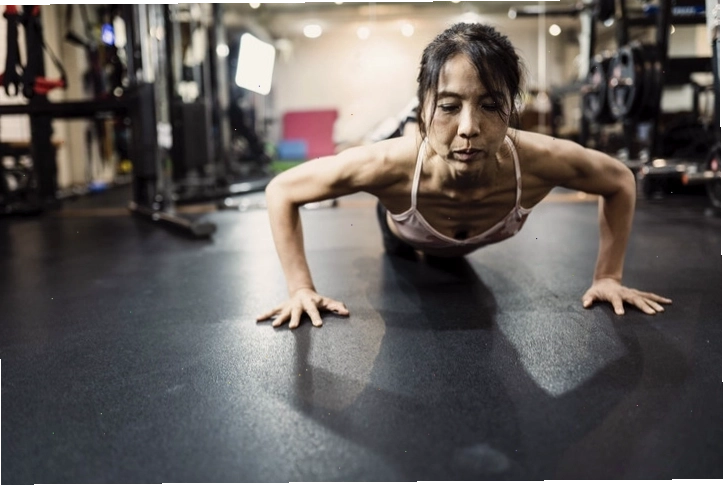 Một phụ nữ châu Á trung niên thực hiện tư thế plank trên sàn phòng gym