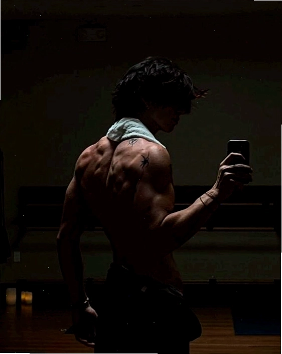 Nam gymer đứng hơi quay lưng về phía gương khoe bờ vai và cơ bắp