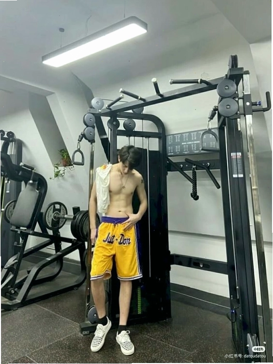 Nam gymer đứng một tay chống bụng, một tay duỗi, đầu cúi nhẹ, chân nhón một bên