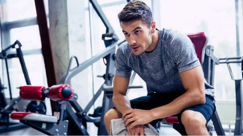 Nam gymer ngồi nhìn xa xăm, người khom, hai tay đan vào nhau qua đầu gối