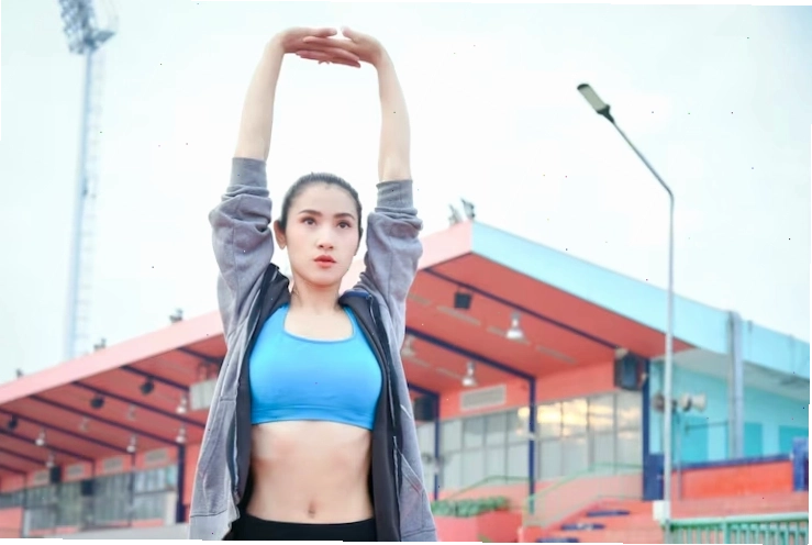 Người phụ nữ châu á xinh đẹp mặc đồ thể thao khởi động trước khi chạy bộ ngoài trời trong thành phố.