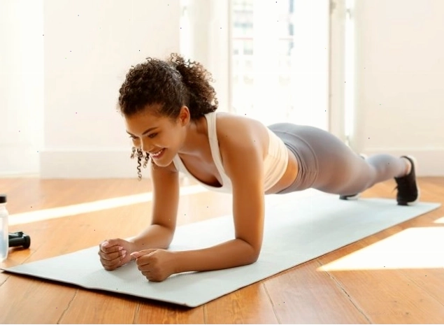 Người phụ nữ trẻ tập thể dục mặc đồ thể thao đang tập plank khuỷu tay để tăng cường sức mạnh cốt lõi trên thảm tập thể dục trong phòng khách hiện đại tại nhà. Khái niệm tập luyện lành mạnh trong nhà, giữ plank.