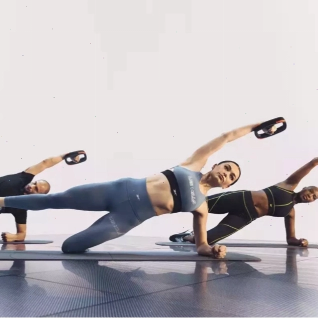 Nhóm người lớn thực hiện tư thế plank nghiêng giữ tạ tay trong lớp thể dục nhóm LES MILLS CORE