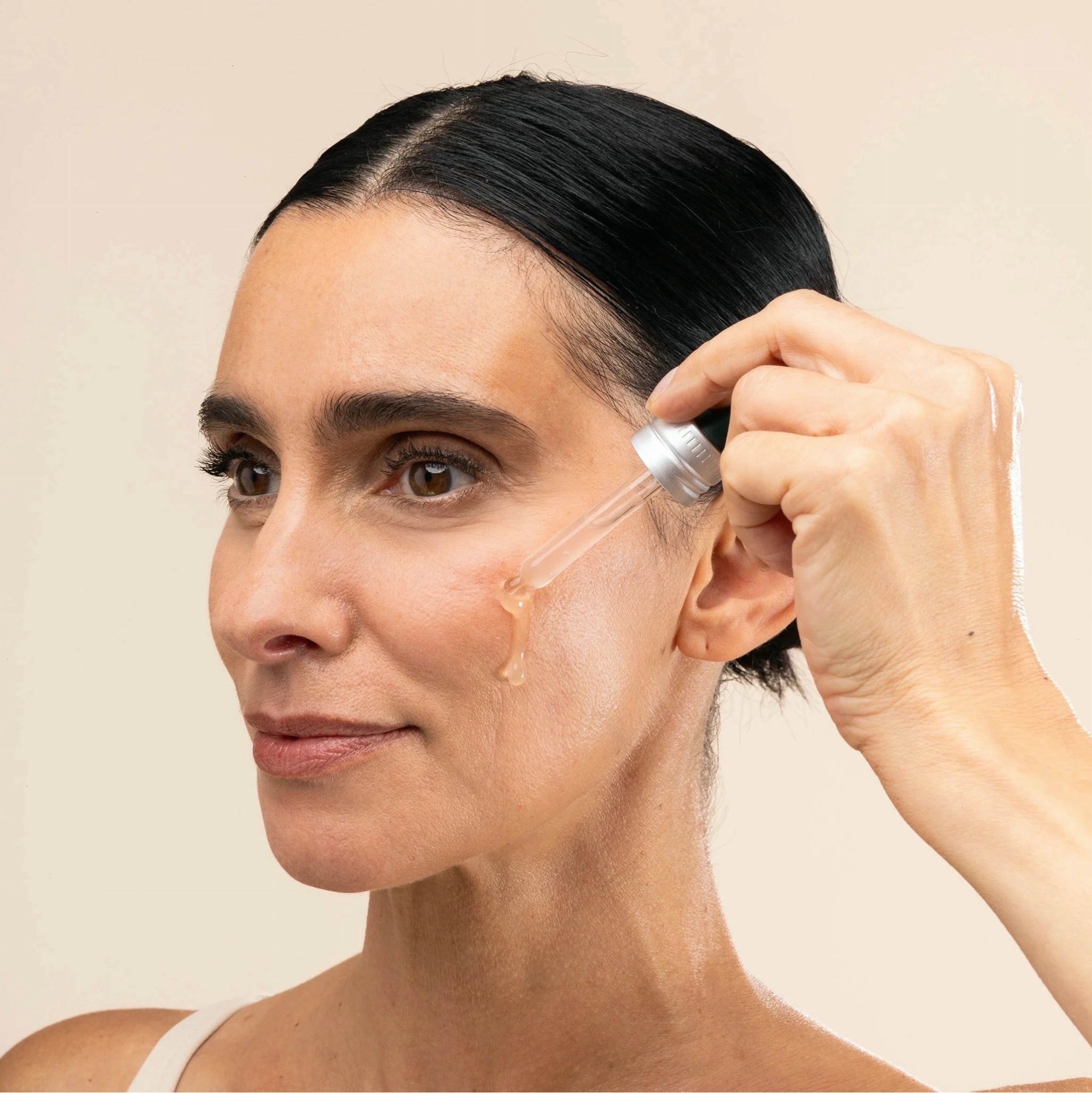 Woman applying Edelweiss Serum to her face with a dropper on a beige background